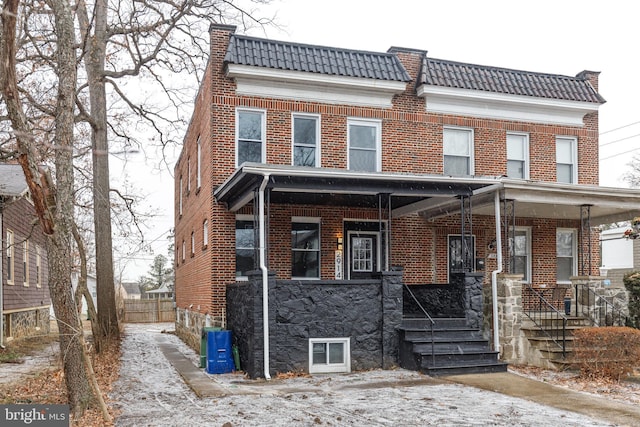 multi unit property featuring covered porch, a tile roof, a chimney, and brick siding