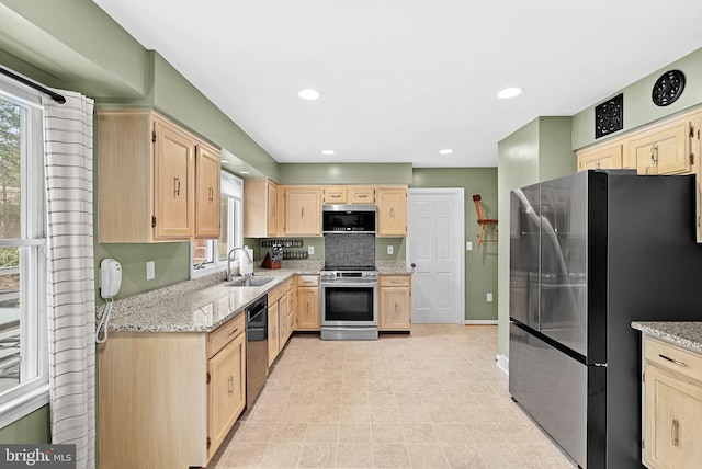 kitchen with stainless steel appliances, light brown cabinets, a sink, and light stone countertops