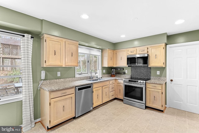 kitchen featuring stainless steel appliances, light stone countertops, a sink, and light brown cabinetry