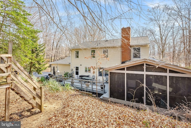 rear view of property featuring a sunroom, a shingled roof, and a chimney