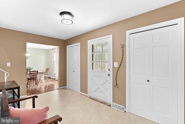 foyer entrance featuring light floors, visible vents, and baseboards