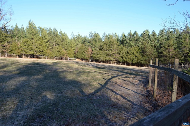 view of yard with a rural view, fence, and a view of trees