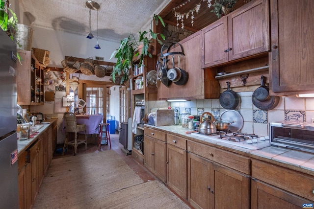 kitchen with tile counters, brown cabinetry, decorative backsplash, white cooktop, and open shelves