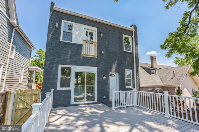 back of house with a wooden deck, brick siding, and fence