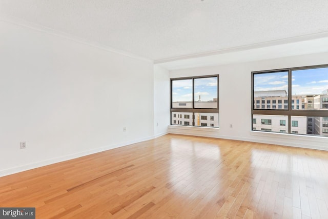 empty room featuring light wood-type flooring, a textured ceiling, and baseboards