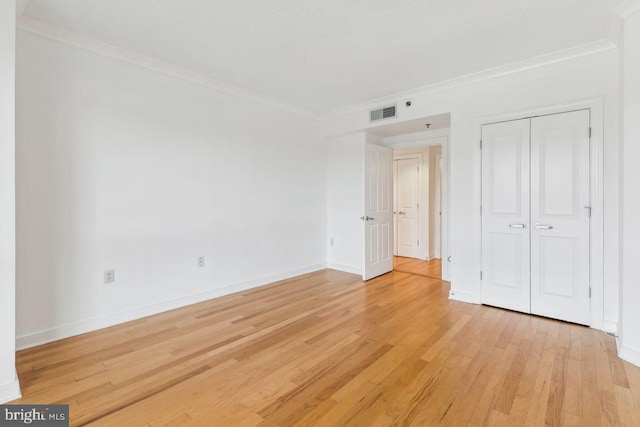 unfurnished bedroom with visible vents, baseboards, light wood-style floors, ornamental molding, and a closet