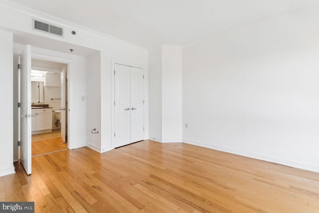 unfurnished bedroom featuring baseboards, visible vents, ornamental molding, light wood-style floors, and a closet