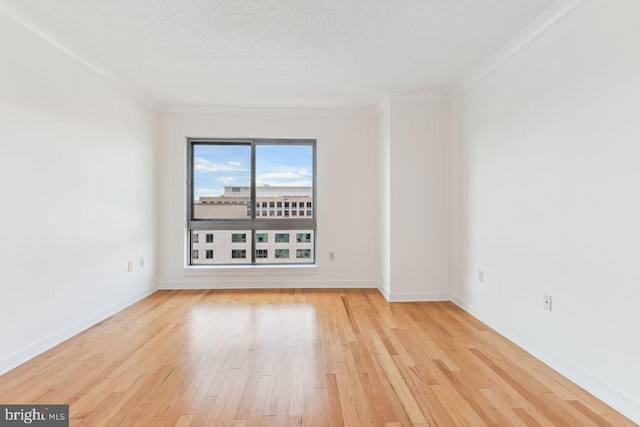 empty room featuring a textured ceiling, light wood finished floors, crown molding, and baseboards