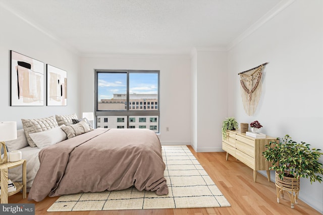 bedroom with light wood-style floors, baseboards, ornamental molding, and a textured ceiling