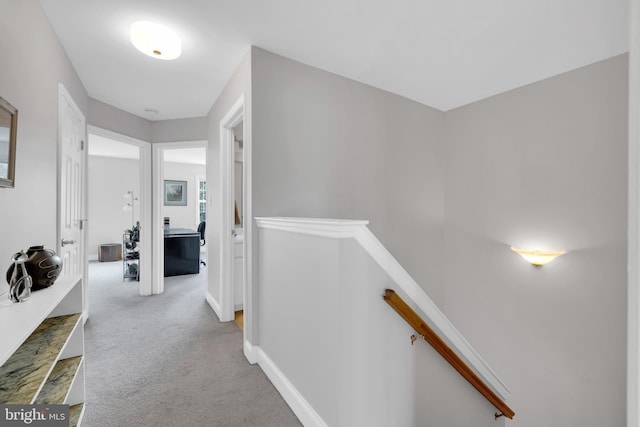 corridor featuring baseboards, an upstairs landing, and light colored carpet