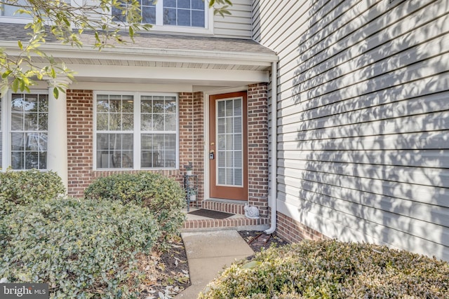 entrance to property with a shingled roof and brick siding