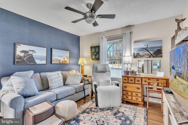 living area featuring light wood finished floors, an accent wall, wallpapered walls, and a textured ceiling