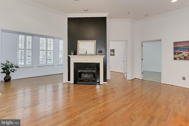 unfurnished living room with light wood-style floors, a high ceiling, ornamental molding, and a fireplace with flush hearth