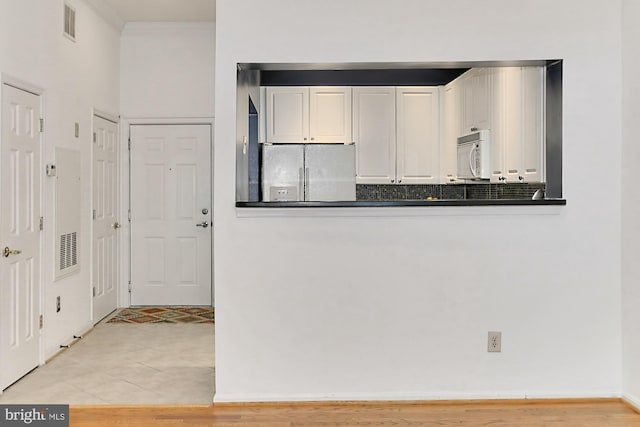 kitchen featuring white microwave, visible vents, ornamental molding, dark countertops, and stainless steel fridge