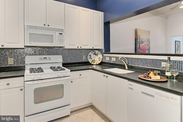 kitchen with light tile patterned floors, white appliances, a sink, white cabinetry, and dark countertops