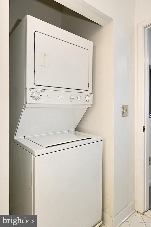 laundry area featuring stacked washing maching and dryer, baseboards, light tile patterned floors, and laundry area