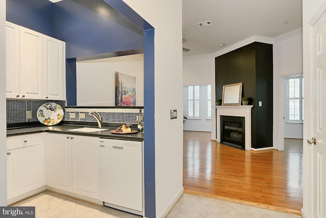 kitchen with white dishwasher, a sink, ornamental molding, backsplash, and dark countertops