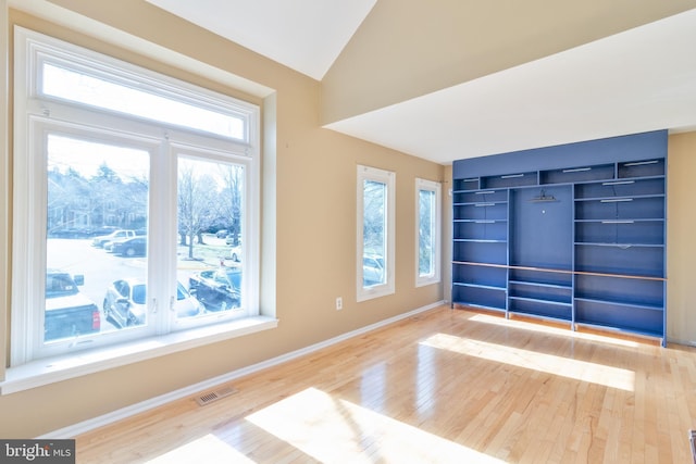 spare room with lofted ceiling, wood finished floors, visible vents, and baseboards