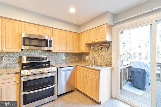 kitchen with light stone counters, stainless steel appliances, a sink, and light brown cabinetry