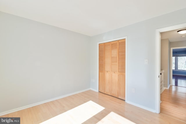 unfurnished bedroom with a closet, light wood-style flooring, and baseboards