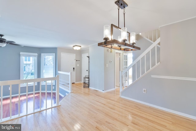 spare room with stairway, baseboards, hardwood / wood-style floors, and ceiling fan with notable chandelier