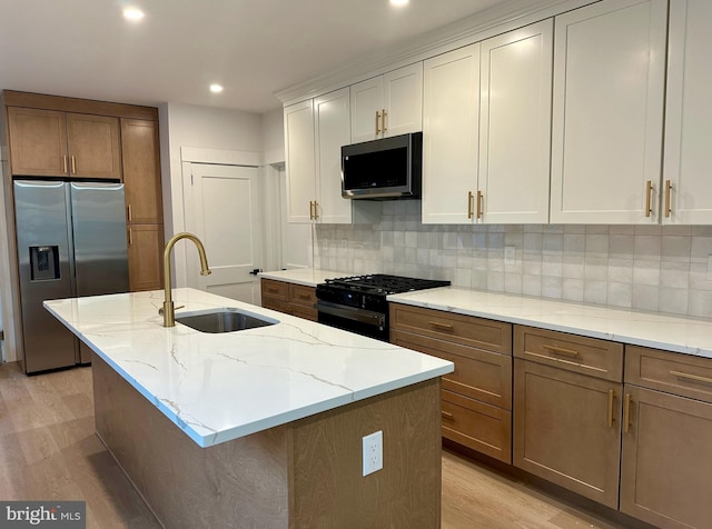 kitchen with light stone counters, stainless steel appliances, backsplash, light wood-style floors, and a sink