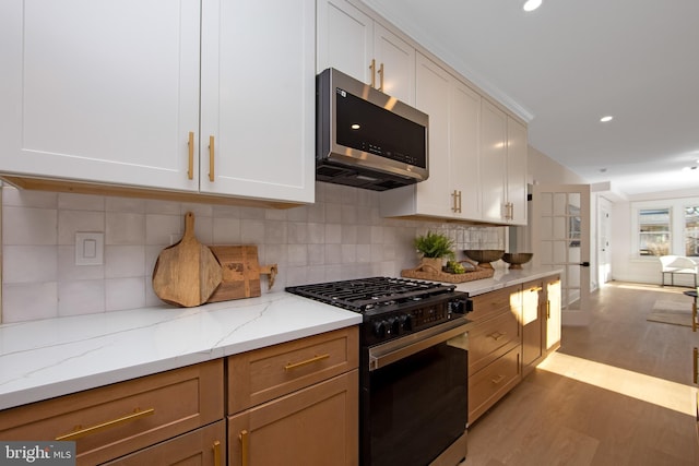 kitchen featuring light wood finished floors, stainless steel microwave, open floor plan, light stone counters, and black gas stove