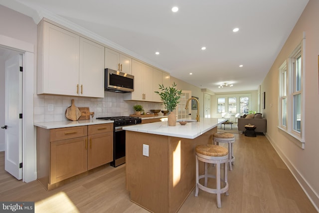 kitchen featuring light wood-style flooring, open floor plan, appliances with stainless steel finishes, tasteful backsplash, and a center island with sink