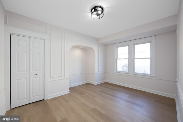 unfurnished room featuring arched walkways, light wood-style flooring, and baseboards