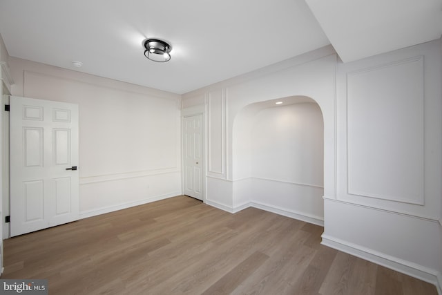 unfurnished room with arched walkways, wood finished floors, and baseboards