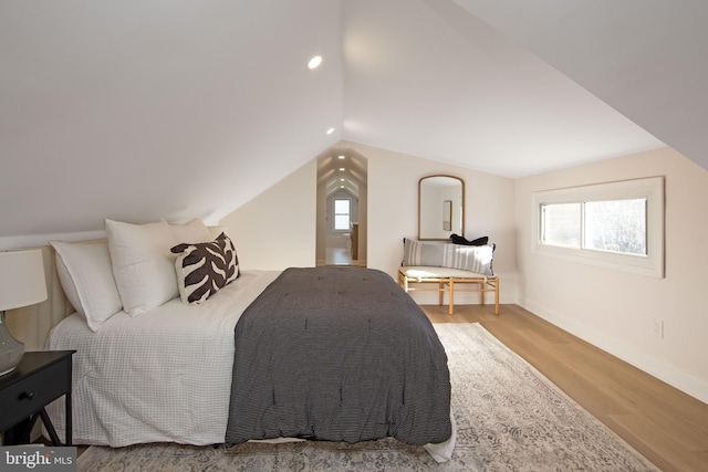 bedroom featuring multiple windows, vaulted ceiling, baseboards, and wood finished floors