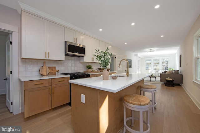 kitchen with a sink, black gas stove, open floor plan, decorative backsplash, and stainless steel microwave