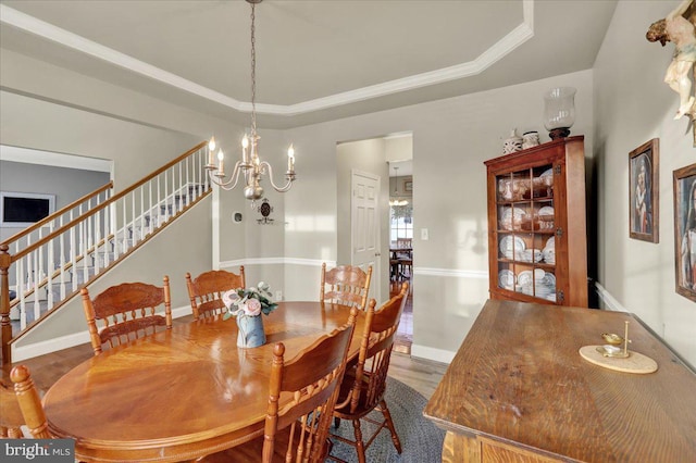 dining space featuring a chandelier, wood finished floors, baseboards, stairs, and a raised ceiling