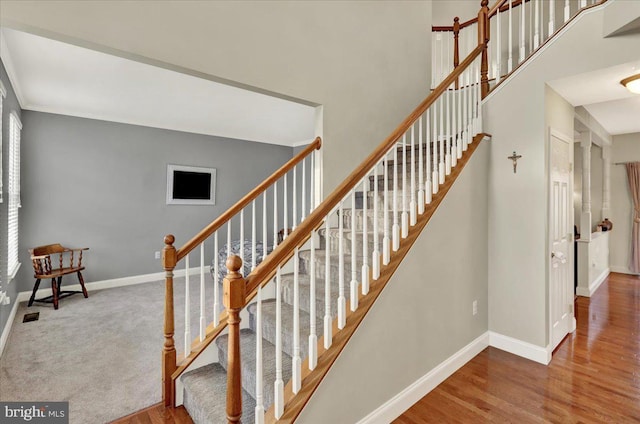 staircase with a towering ceiling, visible vents, baseboards, and wood finished floors