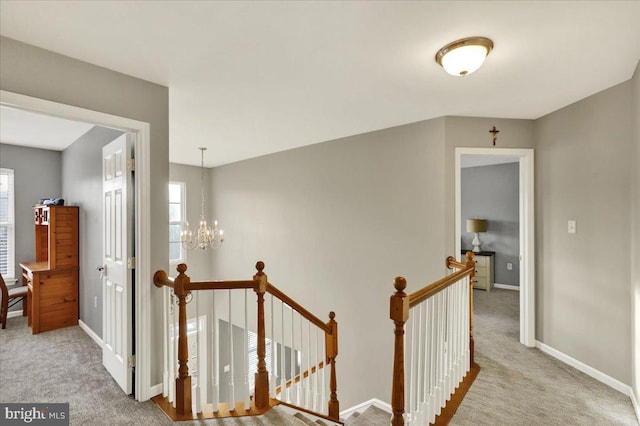 corridor with light carpet, an inviting chandelier, baseboards, and an upstairs landing