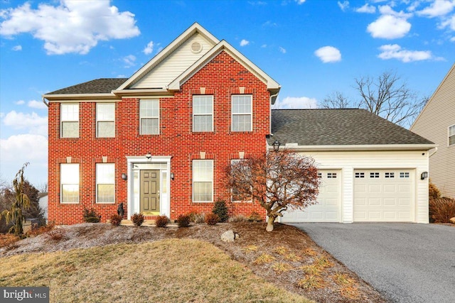 colonial inspired home with a garage, driveway, brick siding, and a shingled roof