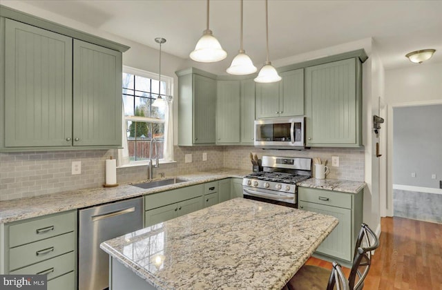 kitchen featuring stainless steel appliances, pendant lighting, green cabinetry, and a sink