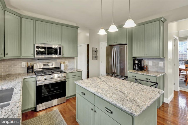 kitchen featuring a kitchen island, appliances with stainless steel finishes, light stone countertops, decorative light fixtures, and green cabinetry