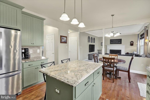 kitchen featuring a center island, decorative light fixtures, freestanding refrigerator, a fireplace, and green cabinetry