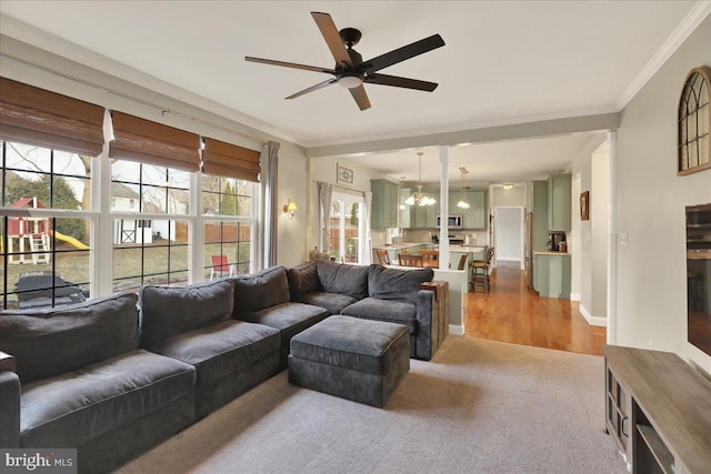 living room with ceiling fan with notable chandelier, ornamental molding, light wood-type flooring, and baseboards