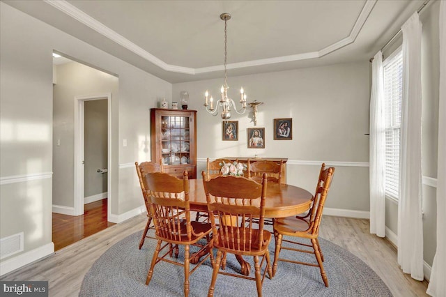 dining area featuring a raised ceiling, visible vents, a notable chandelier, and light wood finished floors