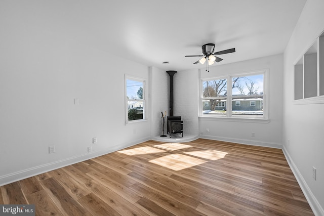 interior space featuring light wood-style floors, a wood stove, ceiling fan, and baseboards