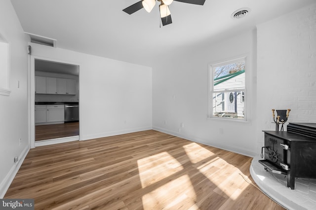 living area featuring a wood stove, baseboards, visible vents, and wood finished floors