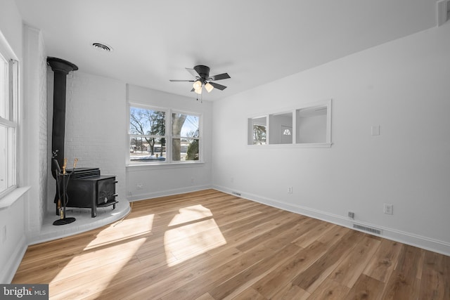 unfurnished living room with visible vents, light wood-style floors, a ceiling fan, a wood stove, and baseboards