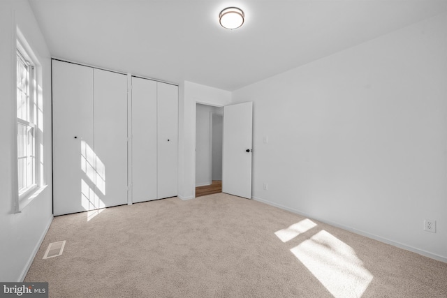 unfurnished bedroom with light carpet, baseboards, visible vents, and two closets