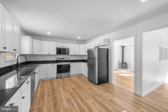 kitchen featuring appliances with stainless steel finishes, a wood stove, light wood-style floors, white cabinetry, and a sink