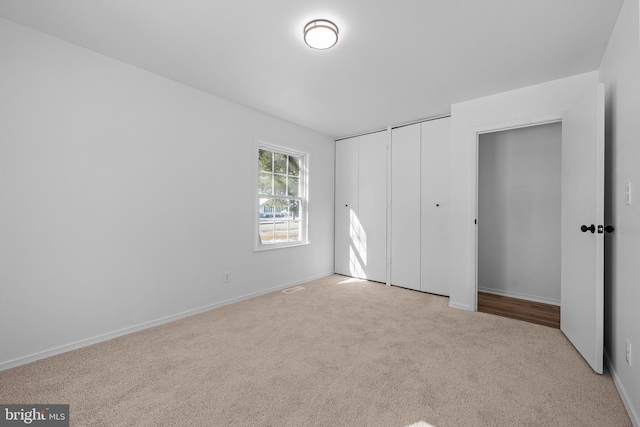 unfurnished bedroom featuring baseboards, visible vents, two closets, and light colored carpet