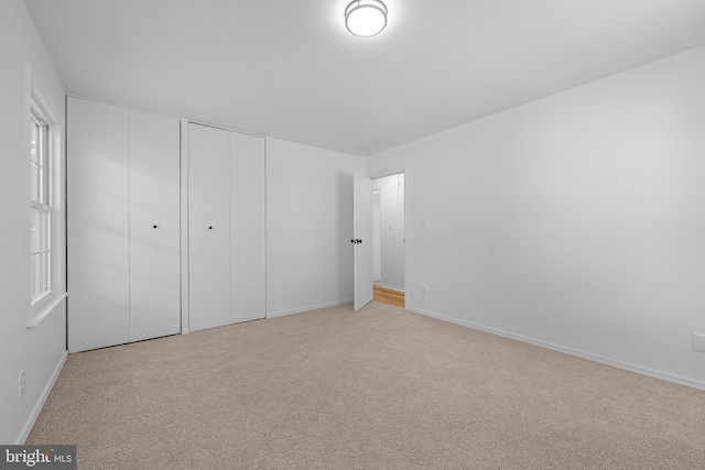 unfurnished bedroom with multiple closets, light colored carpet, and baseboards