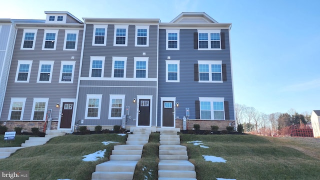 townhome / multi-family property with a front yard, stone siding, and entry steps