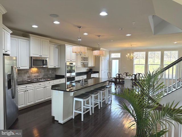 kitchen featuring stainless steel appliances, white cabinets, a kitchen island with sink, and hanging light fixtures